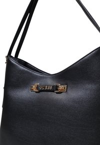Borsa a mano sintetica nera con texture liscia, dotata di un logo in metallo dorato e una silhouette curva e semplice. Due tracolle regolabili.