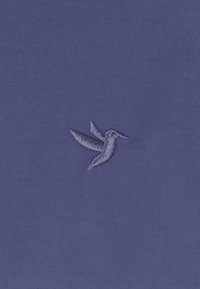 Tessuto blu scuro con una superficie testurizzata, decorato con un piccolo design di un colibrì ricamato in filo azzurro sul lato sinistro.