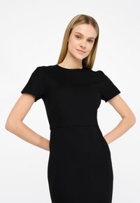 Abito nero aderente con maniche corte, scollo tondo e tessuto morbido. Il design presenta una vita ben definita e una silhouette dritta.