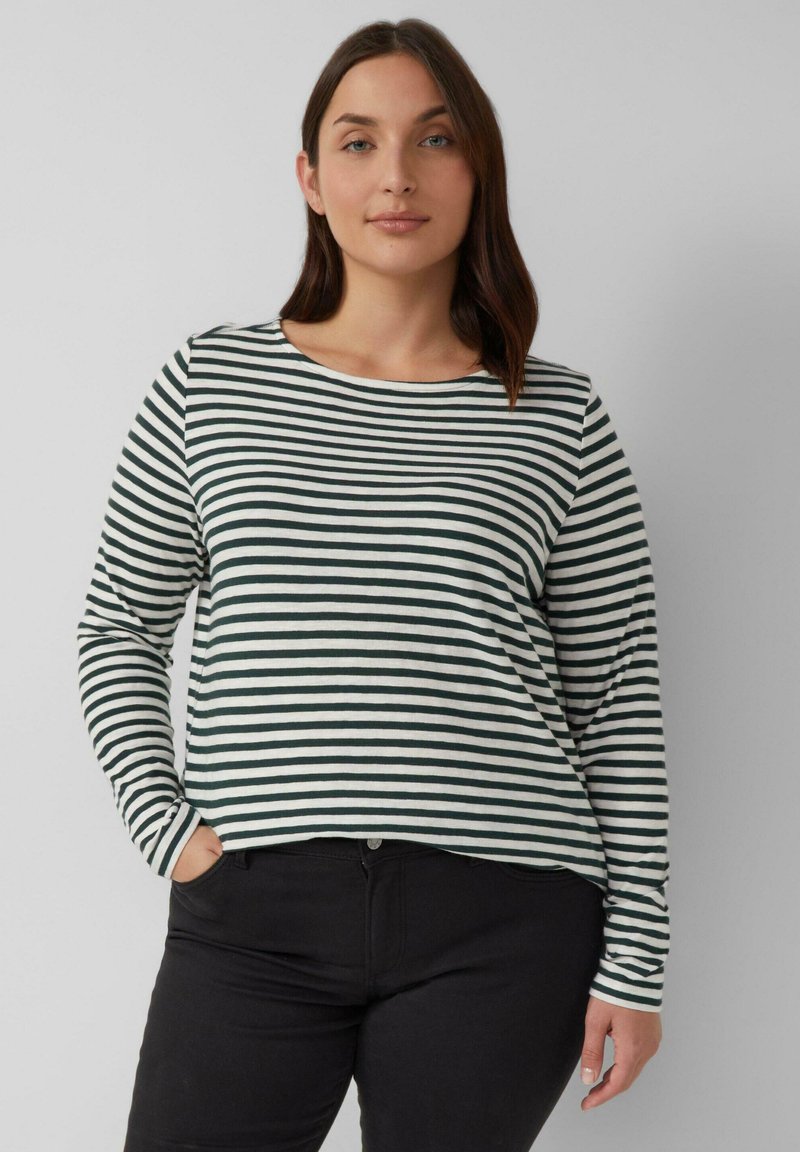 Langsleeve top met witte en donkergroene strepen. Ronde hals, relaxte pasvorm, zachte stof. Gecombineerd met zwarte jeans, handen in de zakken.