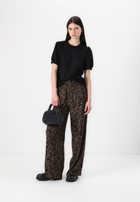 Zwarte textuur top met plooimouwen, gecombineerd met losse broek met luipaardprint. Model houdt een kleine zwarte gevlochten handtas vast en draagt chunky schoenen.