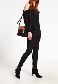 Svart av-axeln-topp, slim-fit svarta byxor och spetsiga svarta anklarstövlar. Accessoar: liten svart handväska med bruna detaljer.