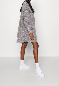 Vestito lungo a maniche lunghe di colore viola con una vestibilità ampia, di lunghezza al ginocchio, abbinato a sneakers bianche e calze alla caviglia. Presenta un tessuto texturizzato.