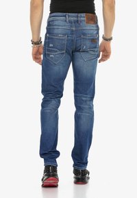 Skinny-fit blauwe spijkerbroek met lichte slijtage, vijf zakken en leren label. Draagt met zwart gestifte schoenen.