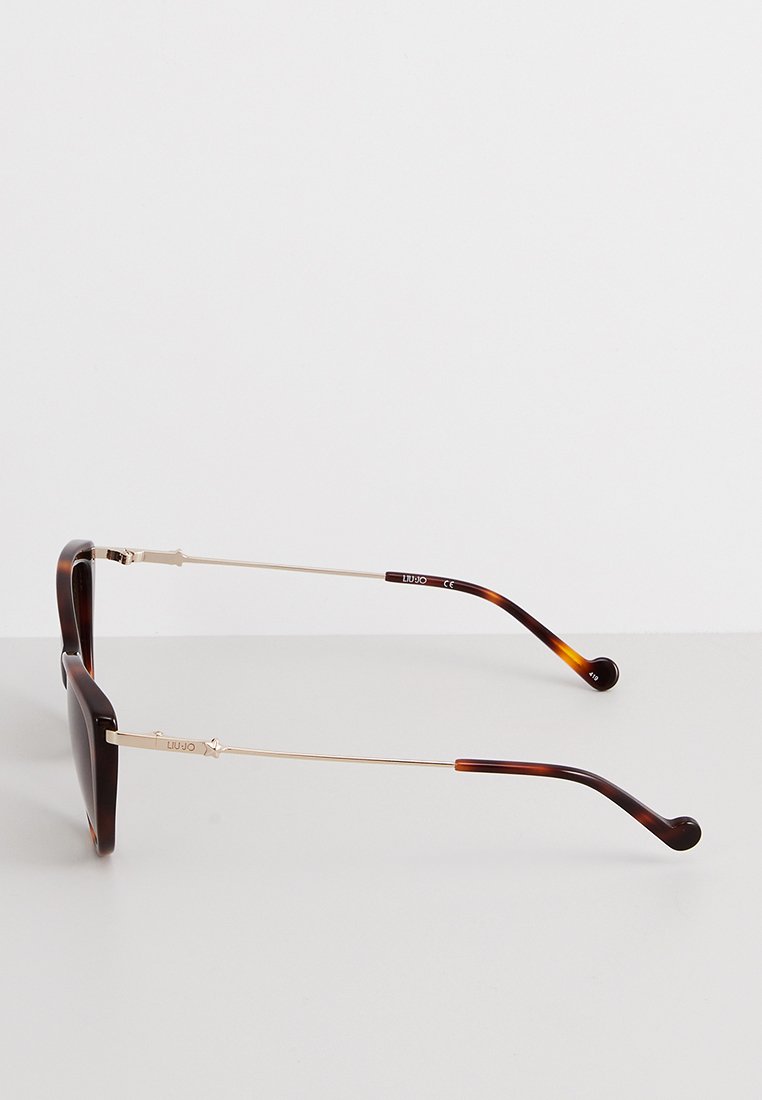 Lunettes de soleil écaille de tortue avec verres sombres, branches en métal doré fines et détails uniques sur le bras. Fini poli, forme rectangulaire.