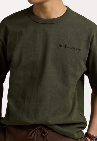 Tricou din bumbac de culoare verde măslin, cu mâneci scurte și guler rotund cu dantelă. Prezentă un logo brodat discret, de culoare neagră, pe piept.