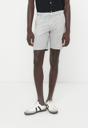 Shorts à motifs gris avec une coupe ajustée, tissu léger et fermeture à boutons, associés à des baskets blanches avec des rayures noires.