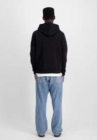 Sort hoodie med en rummelig ryg og hætte, kombineret med løstsiddende lyseblå denimjeans. Glat tekstur, minimalistisk design, ingen synlige mønstre.