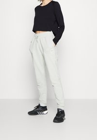 Black cropped long-sleeve top paired with light gray jogger pants featuring side pockets and a small label patch. Black athletic shoes.