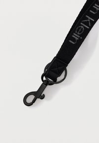 Μαύρο υφασμάτινο κορδόνι με τυπωμένο κείμενο και μαύρο μεταλλικό γάντζο με περιστρεφόμενο κούμπωμα σε λευκό φόντο.