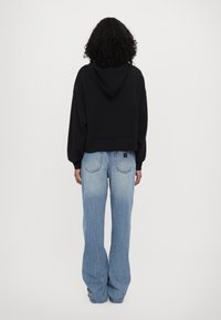 Black cropped hoodie with a drawstring hood, paired with light blue wide-leg jeans featuring a faded texture and back pockets.