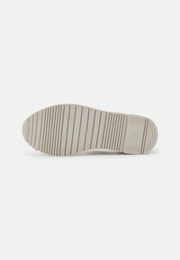Suela de zapato de goma gris claro con surcos horizontales, bordes redondeados y una impresión de logotipo circular. Superficie plana y texturizada para un mejor agarre.