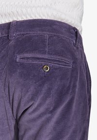 Lilla corduroy bukser med en vertikal ribbet tekstur. Har en baglomme med knaplukning. Stoffet er blødt og robust.
