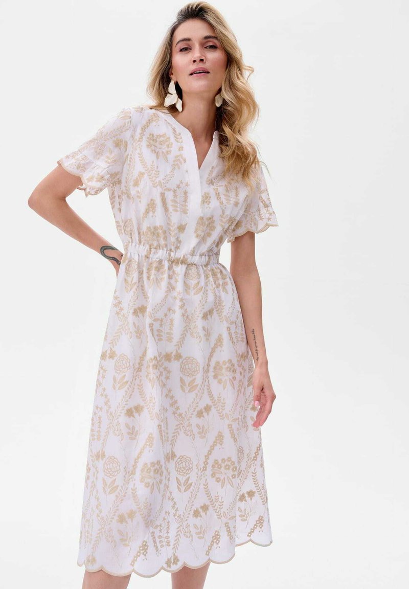 Witte jurk met gouden bloemenpatroon, korte mouwen, V-hals en elastische taille. De gegolfde zoom voegt detail toe aan het halflange ontwerp.