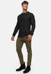 Sort struktureret striktrøje med rund hals, parret med olivengrønne slim-fit bukser og sorte ruskinds ankelstøvler.