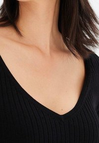 Svart ribbad stickad topp med V-ringning. Har en strukturerad yta och en figurnära silhuett. Halvlånga ärmar och mjuk tyg.