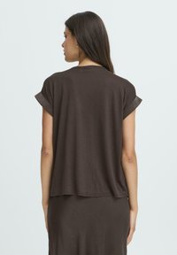 Brun bomulds t-shirt med kortellede ærmer, afslappet pasform og rundet kant. Stoffet ser blødt og let ud. Vist fra ryggen.