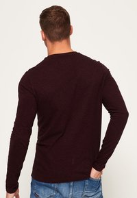 Maroon pitkähihaisuus paita, joka on valmistettu teksturoidusta kankaasta, klassisella pyöreällä pääntiellä ja suoralinjaisella istuvuudella, esiteltynä takaviistosta.