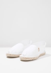 White canvas espadrilles with a rounded toe, natural jute rope sole, and subtle stitched detailing along the edge.