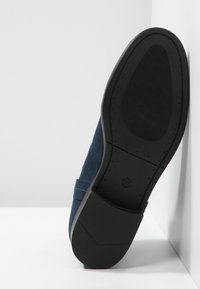 Chaussure en suede bleu avec une semelle en caoutchouc noir texturé. Détails de couture sur le côté et marquage de taille "37" visible sur la semelle.