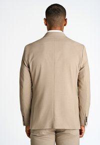 Giacca da abito beige con una texture liscia, vestibilità sartoriale e cuciture sottili. Presenta polsi button-down e uno spacco singolo sul retro.