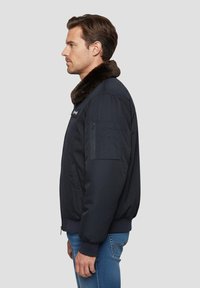 Giacca bomber blu navy con collo in pelliccia sintetica, tasca con zip sulla manica, polsini e orlo a costine. Tessuto liscio con chiusura a zip.
