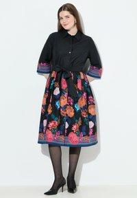 Abito nero con top aderente, motivo floreale in colori vivaci sulla gonna e accenti a righe sulle maniche. Dettaglio in vita legato, lunghezza fino al ginocchio.