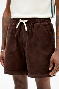 Brune kordfløyelsshorts med elastisk midjebånd og hvit snor. Har sidelommer og en teksturert ribbet overflate.