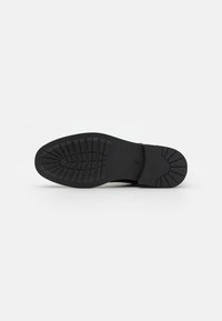 Black rubber sole with textured grip, featuring deep treads and a rounded shape. Smooth edges with no visible markings or logos.