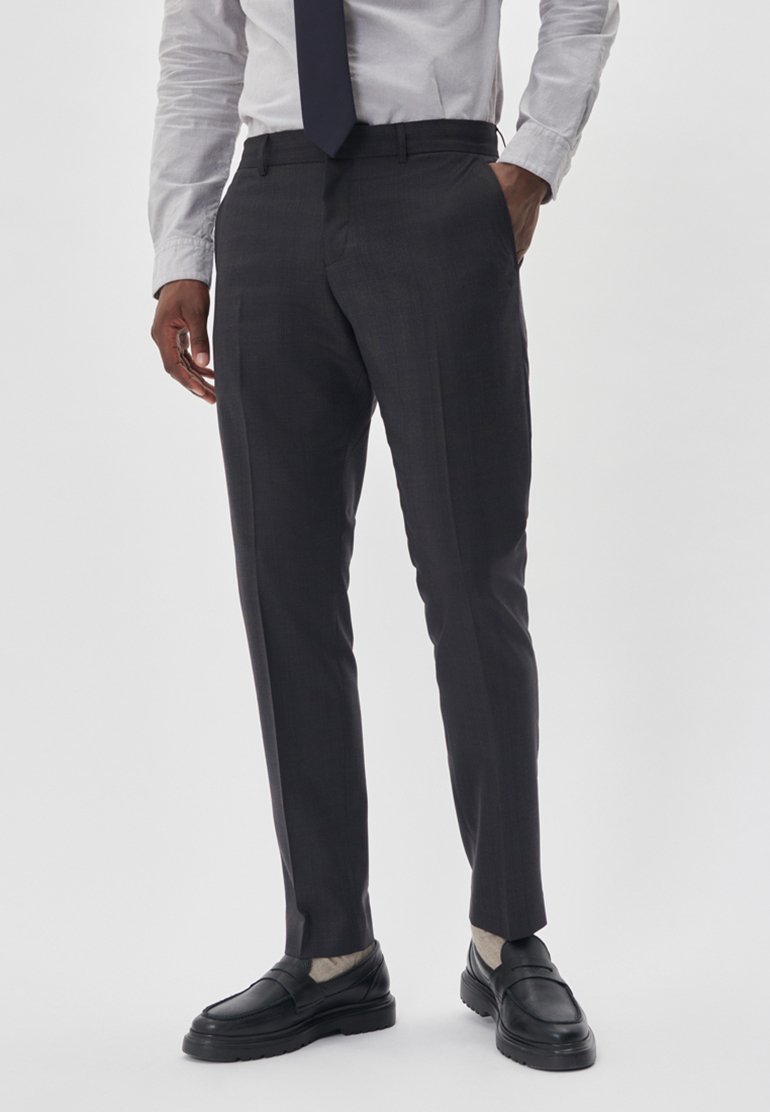 Graue, maßgeschneiderte Hose mit glatter Textur, schmaler Passform und einem einzigem Bundfaltendesign, kombiniert mit einem hellen Hemd und schwarzen Slippern.