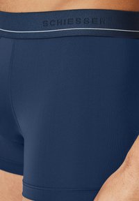 Boxer brevi blu navy con una texture liscia, dotati di un cinturino con marchio e una striscia bianca a contrasto lungo il bordo superiore.