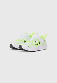 Baskets de sport blanches avec des accents vert fluo et un logo noir. Caractéristiques : tige en maille, sangle à boucle, et semelle en caoutchouc.