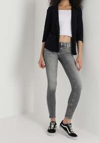 Blazer navy, top corto blanco, jeans skinny grises y zapatillas negras. El blazer tiene un acabado texturizado y bolsillos de parche.