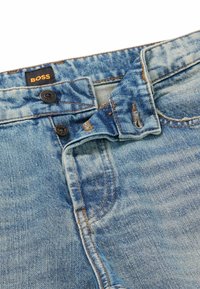 Ljusblå denimjeans med en urtvättad finish, med en knappstängning, kontrasterande sömmar och en svart etikett med "BOSS"-logotypen.