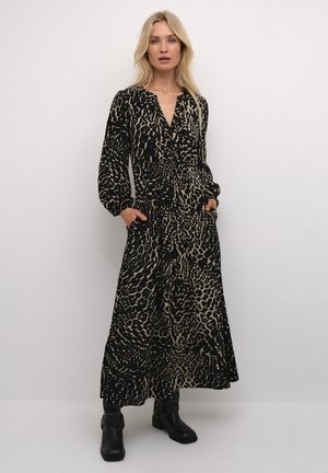Robe à manches longues, à boutons, en imprimé léopard noir et beige, avec une taille cintrée, des poches latérales et une jupe fluide, associée à des bottes noires.