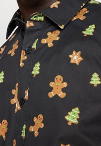 Camicia nera con motivi di pan di zenzero e albero di Natale, caratterizzata da dettagli verdi e marroni, chiusura con bottoni e design classico del colletto.