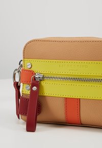 Läderväska i tan med ett gult rand, orange detaljer och silverdragkedja. Inkluderar ett rött rem och metallbeslag för fäste.