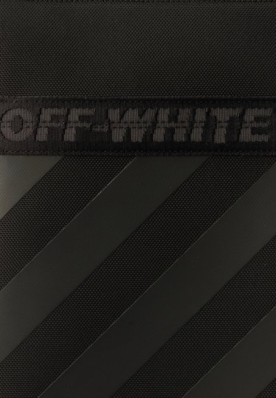 Μαύρη υφή επιφάνειας με διαγώνιες σκοτεινές ρίγες και μια μαύρη υφασμένη ετικέτα με ανάγλυφο το κείμενο "OFF-WHITE."