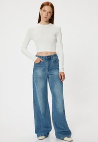 Biała, długourkowa crop top połączony z błękitnymi, jasnymi dżinsami o wysokim stanie i szerokich nogawkach. Gładka tekstura oraz klasyczny pięciokieszeniowy design.
