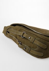 Olivengrüne Wildledertasche mit flachem Design, Metallbeschlägen und kontrastierenden Nähten. Verfügt über einen verstellbaren Gurt mit Schnallen-Details.
