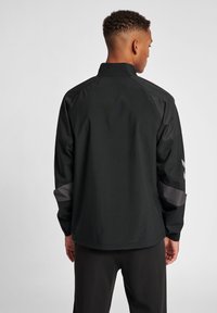 Schwarze Windjacke mit Stehkragen, elastischen Bündchen und kontrastierenden grauen Akzenten an Schultern undÄrmeln. Glattes, leichtes Material.