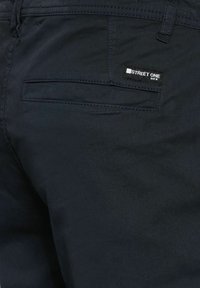 Pantalones de algodón azul marino oscuro con un bolsillo trasero que lleva una etiqueta que dice "STREET ONE". La tela tiene una textura suave y costuras limpias.