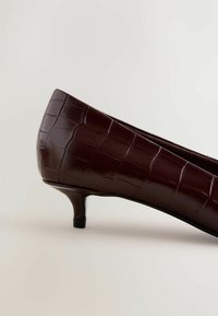 Brūni krokodila raksta iespiesti ādas kurpes ar asu purngalu un 2 collu papēdi. Gluda tekstūra ar spīdīgu apdari un slaids siluets.