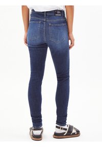 Tmavě modré skinny džíny s klasickým pětivreckovým designem, detailem na zadním sedle a pohodlným pasem. Kombinované s sandály.