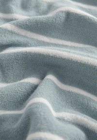 Weiche, strukturierte Handtuch aus hellblauem Stoff mit weißen horizontalen Streifen, die ein leichtes, strukturiertes Aussehen erzeugen.