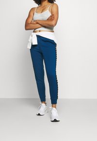 Blå joggerbyxor med svarta sidostrimmor, gjorda av mjukt tyg. Matchas med en ljusgrå crop top och vita sneakers.