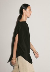 Chemise en lin noire avec une coupe décontractée, des manches surdimensionnées et un col haut. Présente un ourlet en pointe et un détail de drapage subtil.