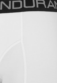 Vita bomullsboxer med svart elastisk midjeband som har texten "ANDURAM" i grått. Sömdetaljer synliga på tyget.