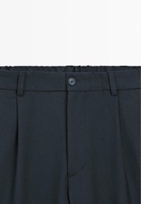 Tmavě šedé kalhoty na míru s hladkou texturou, vybavené širokým pasovým lemem, předními sklady a knoflíkovým zapínáním v pase.