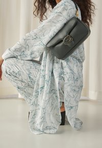 Harmaa nahkalaukku kultaisella yksityiskohdalla, pidettynä marmorikuvioisen vaaleansinisen ja valkoisen asun päällä, jossa on leveät hihat ja housut.